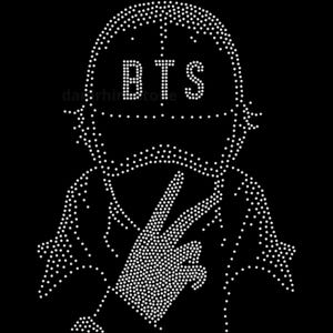 May include: A rhinestone transfer design on a black background featuring a stylized figure wearing a baseball cap with the letters BTS clearly visible. The figure is making a peace sign gesture with one hand, all outlined in small white crystals.