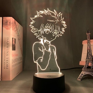 May include: A glowing LED lamp featuring a cartoon character design. The lamp has a black base and a clear, etched figure that illuminates with a bright white light. The design is of a young male character with spiky hair.