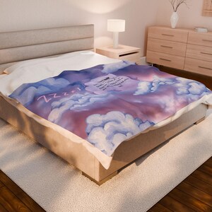 May include: A soft blanket featuring a dreamy cloudscape design in shades of purple, pink, and blue. The blanket has a whimsical feel with the word "Zzz" and a quote about dreams. This cozy blanket is perfect for a bedroom.