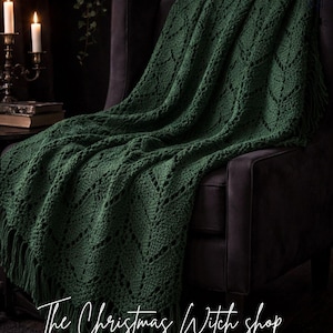 Peut inclure: Une couverture en crochet vert foncé avec un motif en losange et des franges est drapée sur un fauteuil sombre. La couverture est au centre de l'image, avec le texte "The Christmas Witch shop" et "Crochet Patterns & Spooky Vibes" en bas.