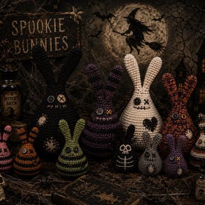 Puede incluir: Una colección de figuras de conejos de ganchillo hechas a mano en varios tamaños y colores, incluyendo negro, morado, naranja y verde. Los conejos tienen ojos de botón y detalles cosidos, con un tema de Halloween. El fondo incluye un letrero que dice "Spookie Bunnies".