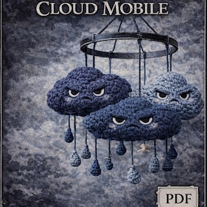 Op de afbeelding: Een handgemaakte gehaakte mobiel met drie humeurige stormwolken in blauwtinten, elk met geborduurde ogen en hangende druppels. De mobiel hangt aan een metalen ring. De tekst op de afbeelding luidt "Grumpy Storm Cloud Mobile" en "Crochet Pattern".
