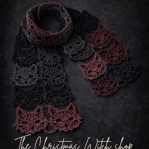 May include: A crocheted scarf featuring a cat face design in black, grey, and burgundy hues. The scarf is shown against a dark backdrop. The image includes the text "Enchanted Cat Lace Scarf pattern" and "The Christmas Witch shop".