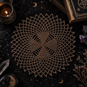 May include: A brown, crocheted doily with a circular, openwork design. The doily is centered on a black surface with celestial patterns, alongside a lit candle, crystals, and antique books. The intricate pattern and warm color create a vintage aesthetic.