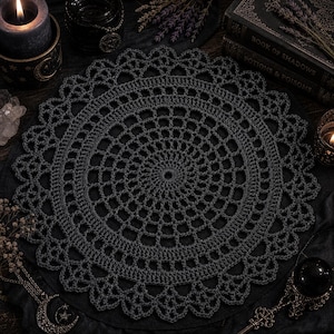 May include: A dark gray, circular crochet doily with a detailed openwork design. The doily features a scalloped edge and a spiral center. The image has a gothic or witchy theme, with candles, books, and crystals in the background.