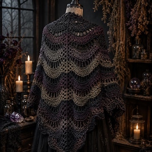 May include: A multi-coloured crochet shawl, displayed on a mannequin. The shawl has a scalloped edge and a gradient of colours, including black, purple, and gold. The background includes candles, a dark window, and decorative items.