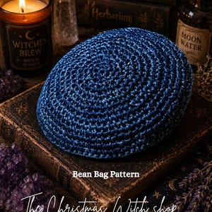 May include: A dark blue, crocheted bean bag pattern sits atop a vintage book. The image includes a lit candle, crystals, and bottles with labels. Text on the image reads "Bean Bag Pattern" and "The Christmas Witch shop".