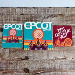 May include: Three vintage EPCOT Center brochures on a wooden surface. The brochures feature the EPCOT Center logo with a geometric sphere and a stylized building. One brochure reads "Tips on Your Visit."