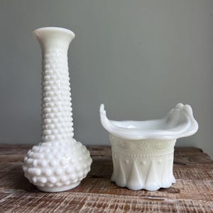 May include: A tall white milk glass vase with a hobnail texture and a shorter white milk glass bowl featuring a ruffled top edge and a decorative embossed pattern of dots and triangles around the exterior surface of the vessel.