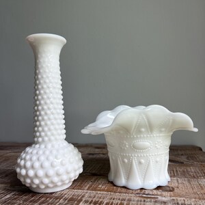 May include: A tall white milk glass vase with a hobnail texture and a shorter white milk glass bowl featuring a ruffled rim and a decorative pattern of embossed dots, ovals, and vertical lines around the exterior of the vessel.