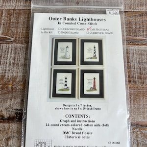 Op de afbeelding: Een kruissteekpakket met Outer Banks vuurtorens. De kit bevat aida-stof, naald, DMC-garens en instructies. Het ontwerp is 12,7 x 17,8 cm en wordt getoond in een lijst van 20,3 x 25,4 cm. Bevat vuurtorens van Cape Hatteras, Ocracoke Island, Bodie Island en Currituck Beach.