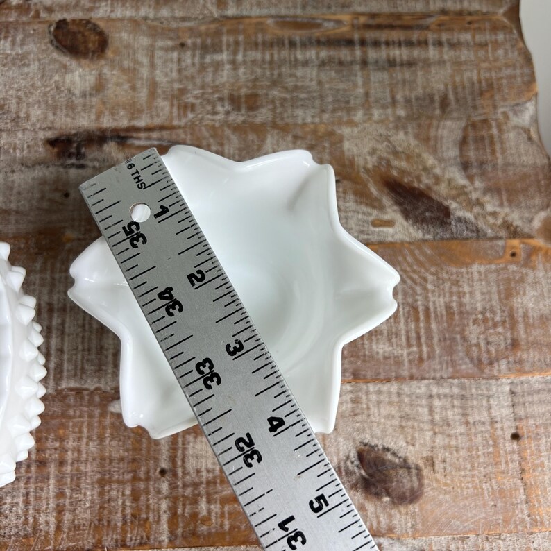 May include: A white star-shaped ceramic dish with a smooth finish. A metal ruler is placed across the center, showing a diameter of approximately 3.5 inches. The dish features five distinct points and a central basin for holding small items.