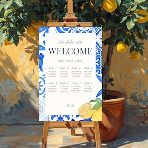 Może przedstawiać: Znak powitalny z niebiesko-białymi wzorami dekoracyjnymi i napisem "La dolce vita WELCOME FIND YOUR TABLE". Znak znajduje się na drewnianym sztaludze, z drzewem cytrynowym w tle.