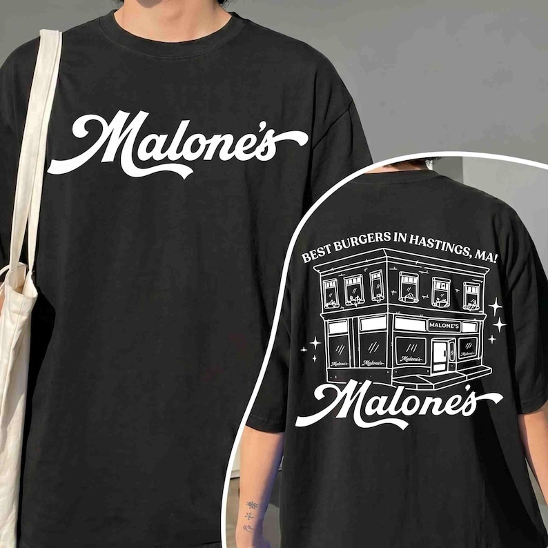 May include: Black t-shirt with the white text "Malone's" on the front. The back of the shirt features a white illustration of a building with the text "Best Burgers in Hastings, MA!" and "Malone's".