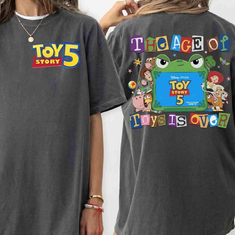 Pode incluir: Uma t-shirt cinzento-carv&atilde;o com um pequeno log&oacute;tipo Toy Story 5 no peito esquerdo. As costas apresentam um gr&aacute;fico grande com uma moldura de sapo verde, v&aacute;rias personagens de Toy Story e o texto The Age of Toys is Over em letras coloridas.