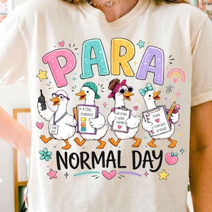 May include: A cream-colored t-shirt featuring a graphic of four cartoon ducks dressed as professionals. The text "PARA" appears above the ducks and "NORMAL DAY" below. The ducks hold clipboards and wear accessories like glasses and hats.