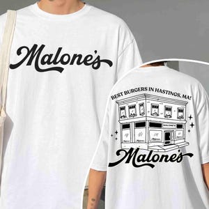 May include: White t-shirt with the word "Malone's" in black script on the front. The back features a black and white illustration of a building with the text "Best Burgers in Hastings, MA!" and the "Malone's" logo.