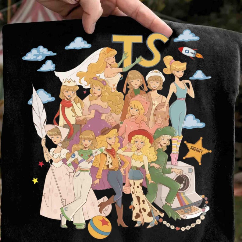 May include: A black t-shirt featuring a graphic print of multiple blonde characters in various outfits, including a space suit, cowgirl attire, and formal gowns. The design includes blue clouds, a rocket, a yellow star badge labeled SHERIFY, and the letters TS.