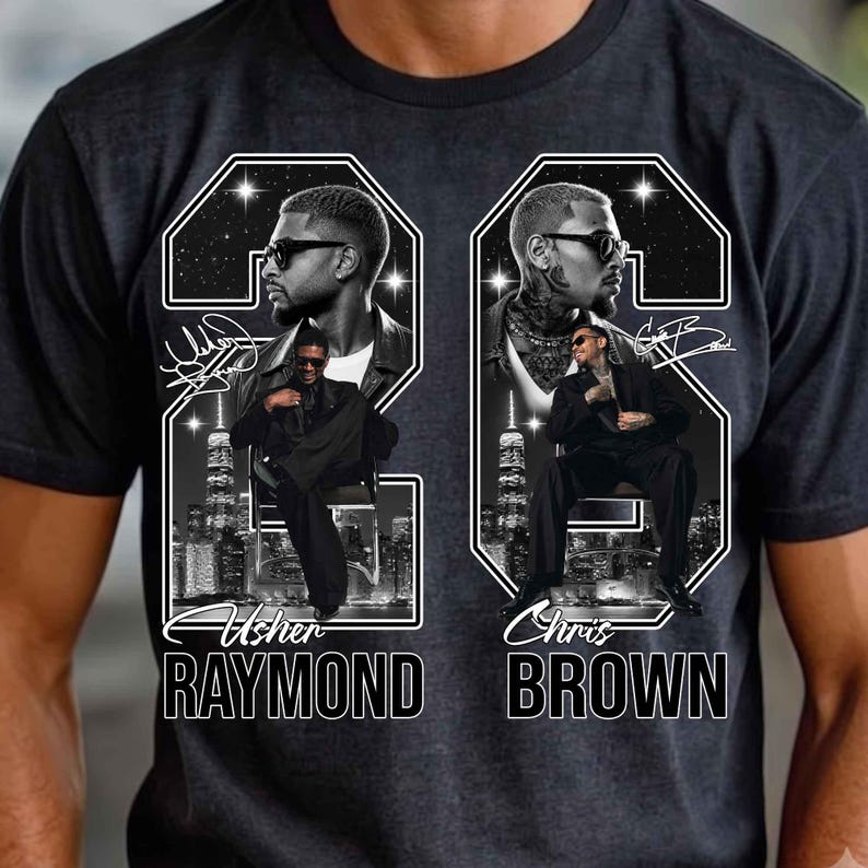 May include: A charcoal gray t-shirt featuring a graphic print of Usher Raymond and Chris Brown. The design includes two large numbers, portraits of the artists wearing sunglasses, city skylines, star patterns, and their names printed in white.