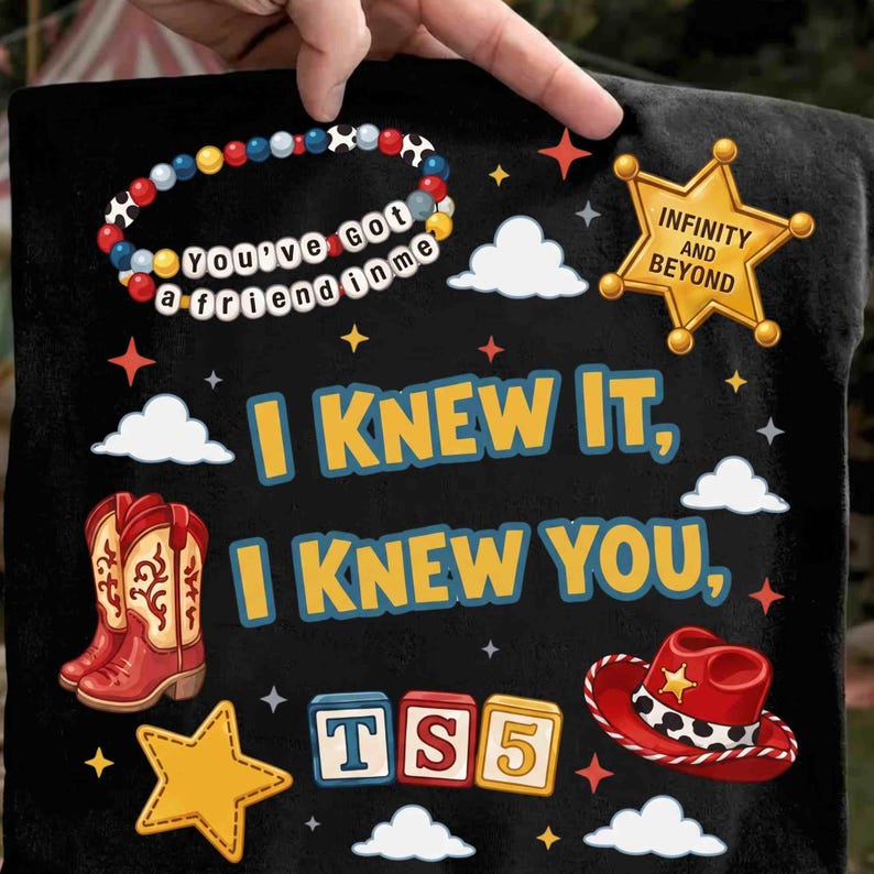 May include: A black t-shirt featuring a graphic print with the text "I KNEW IT, I KNEW YOU," a beaded bracelet with "YOU'VE GOT A FRIEND IN ME," a gold sheriff badge with "INFINITY AND BEYOND," red cowboy boots, a red cowboy hat, and "TS5" blocks.