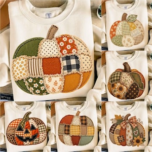 Puede incluir: Una sudadera de cuello redondo color crema con un gran aplique central de calabaza hecho de varios parches de tela. El diseño de la calabaza incluye diversos patrones como flores, cuadros, lunares y pana en tonos naranja, verde y marrón.