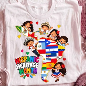May include: A white t-shirt featuring a colorful graphic of the map of Latin America composed of various national flags. Several cartoon children are positioned around the map. The text "HISPANIC HERITAGE MONTH" is printed in multi-colored letters.