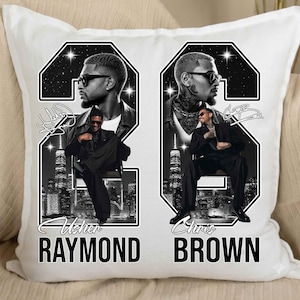May include: A white square throw pillow featuring a black and white graphic design. The print displays two large numbers, 2 and 6, framing portraits of Usher Raymond and Chris Brown. Each artist is shown in a suit, with city skylines and text below.