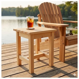 Puede incluir: Una mesa auxiliar de madera de color claro con una bebida encima, junto a una silla Adirondack de madera. La mesa es cuadrada, con una parte superior de listones y cuatro patas robustas. La silla tiene un respaldo alto y amplios reposabrazos. La escena está ambientada al aire libre, cerca de un lago.