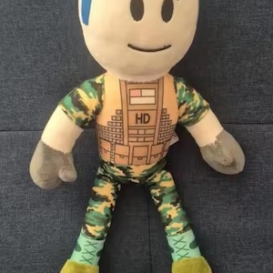 May include: A plush doll with a light skin tone, blue hair, and a smiling face. The doll wears a camouflage-patterned outfit with the letters "HD" on the chest. The doll's hands are gray, and the feet are yellow.
