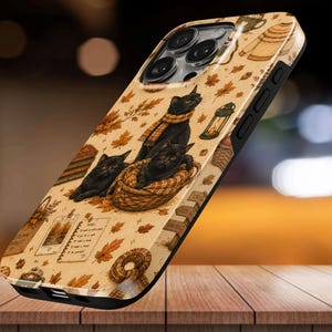Puede incluir: Una funda para smartphone con fondo beige y un patrón de gatos negros, hojas de otoño, una cesta tejida, una linterna, un suéter y una página de cuaderno con texto escrito a mano. La funda tiene un marco negro y una abertura para la cámara.