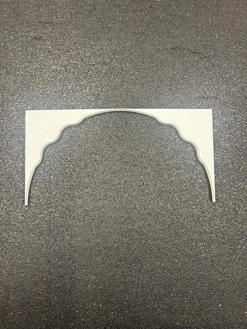 May include: A flat, off-white decorative arch piece featuring a scalloped, curved inner edge and straight outer vertical sides. The object is composed of two symmetrical halves joined at the center, creating a wide, continuous arched opening.