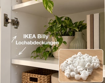 May include: A collection of small, round, white plastic hole covers designed for furniture shelf adjustment holes. The image shows these covers installed in a white cabinet interior and a separate inset view of a pile of the loose white plastic caps.