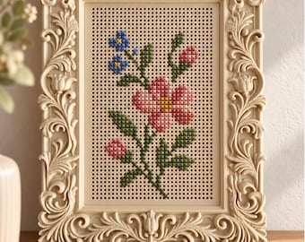 May include: A rectangular cream-colored frame with ornate carved scrollwork borders a perforated panel featuring a cross-stitch floral design. The embroidery displays a large pink flower, smaller pink buds, green leaves, and small blue blossoms.