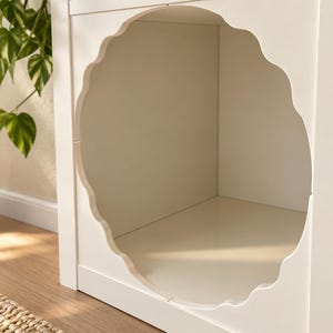 May include: A white storage unit featuring a square cubby with a scalloped, circular cutout opening. The interior of the cubby is smooth and white, providing an open space for storage or display within the structured frame of the furniture piece.