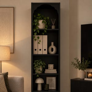 May include: A tall, black, narrow bookshelf with an arched top design featuring five shelves. The shelves are filled with various decorative items including potted green plants, three beige ring binders, a ceramic vase, and a small table lamp.