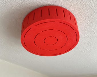May include: A bright red, circular, flat-topped ceiling mount cover with a textured surface. The cylindrical side features vertical slots, while the circular face displays concentric rings of dashed cutouts for ventilation.
