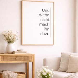 Peut inclure: Une affiche encadrée avec le texte allemand "Und wenn nicht mach ihn dazu" en noir sur fond blanc. L'affiche est accrochée au-dessus d'une table en bois avec un vase blanc de fleurs séchées. Un canapé et des fleurs supplémentaires sont également visibles.
