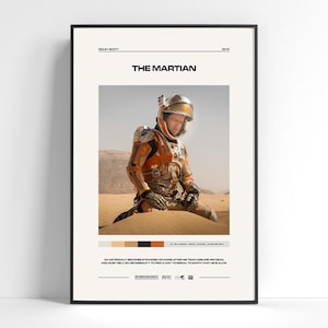 May include: A framed movie poster for The Martian featuring an astronaut in an orange and white space suit kneeling in a desert landscape. The poster includes the title, director Ridley Scott, the year 2015, a color palette, and a plot summary.