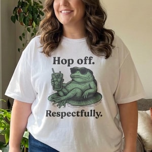 May include: White t-shirt with a graphic of a frog wearing sunglasses and holding a drink, lounging on a lily pad. The text "Hop off. Respectfully." is printed below the frog.