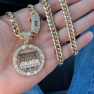 Può includere: Set di collana e bracciale a catena dorata. La collana presenta un grande pendente rotondo con un design dettagliato dell'Ultima Cena, circondato da piccole pietre trasparenti. Le maglie della catena sono spesse e rettangolari.
