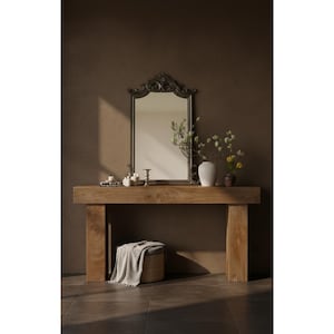 May include: A wooden console table with a decorative mirror, vases, and candles. The mirror has an ornate, dark frame. A small stool with a blanket is placed beneath the table. The room has a warm, neutral color palette.