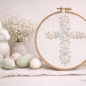 May include: Embroidered cross with pastel flowers in a wooden hoop. A white ceramic rabbit, speckled Easter eggs, and baby's breath flowers are arranged nearby. The text "Little Sparrow Co." is at the bottom.