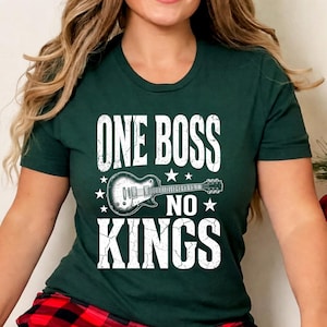 May include: Dark green t-shirt with the text "ONE BOSS NO KINGS" in distressed white lettering. A black and white guitar graphic is centered below the words. The shirt has a round neckline and short sleeves.