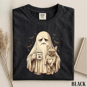 Könnte beinhalten: Ein schwarzes T-Shirt mit einer Grafik eines traurigen Geistes, der eine dampfende Tasse mit der Aufschrift MEH und einem Kürbis-Symbol hält, während er eine französische Bulldogge trägt. Der Geist ist von kleinen Sternen und Fledermäusen umgeben.