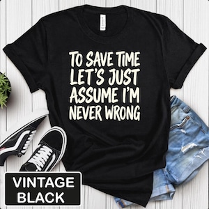 May include: A black short-sleeved t-shirt featuring the white text "TO SAVE TIME LET'S JUST ASSUME I'M NEVER WRONG" printed in a bold, sans-serif font on the chest. The garment has a crew neckline and is displayed alongside black and white sneakers.