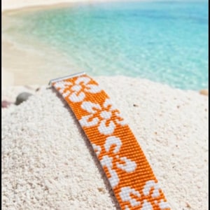 May include: A woven seed bead bracelet featuring a repeating floral pattern in vibrant orange and crisp white. The rectangular band is finished with silver-toned metal end bars and a delicate chain link closure, creating a structured accessory.