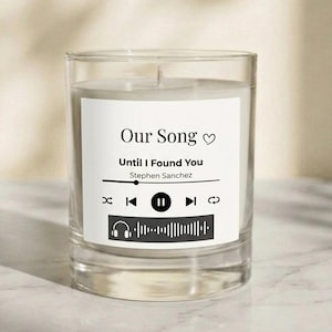 Puede incluir: Una taza de cerámica blanca con asa negra y el texto "But First, Coffee" en negrita negra. La taza se encuentra sobre un fondo borroso, sugiriendo un ambiente acogedor.