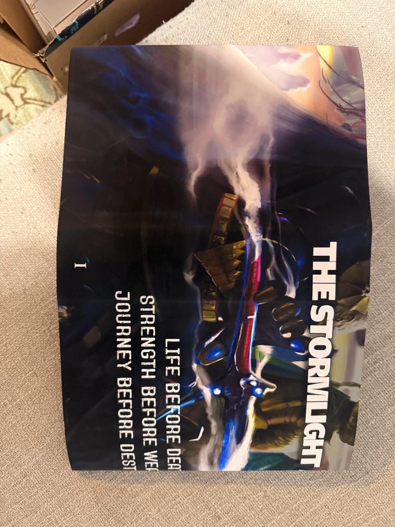 Puede incluir: Portada del libro "The Stormlight Archive" con una ilustraci&oacute;n de fantas&iacute;a. La portada presenta una escena oscura y dram&aacute;tica con una figura sosteniendo un arma brillante. El texto incluye "The Stormlight Archive" y "Life Before Death".