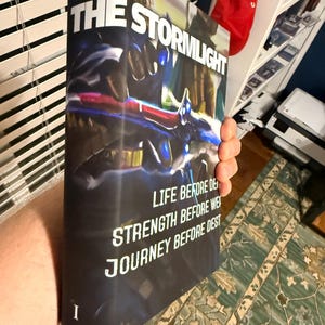 Puede incluir: Un libro de tapa dura titulado "The Stormlight Archive" con una cubierta oscura que presenta un dise&ntilde;o futurista en azul, rojo y blanco. El lomo del libro muestra el t&iacute;tulo y las frases "Life Before Death", "Strength Before Weakness" y "Journey Before Destination".