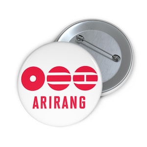 May include: White button with a red design and the word "ARIRANG" in red. The design consists of three red circles, each with a different pattern. One button is shown face up, and another is shown face down.